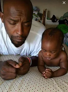 A man and baby laying on the floor.